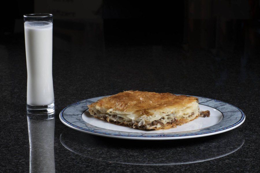 Ein Stück Burek liegt auf einem Teller neben einem Glas Milch. Foto von der Burek House GmbH.