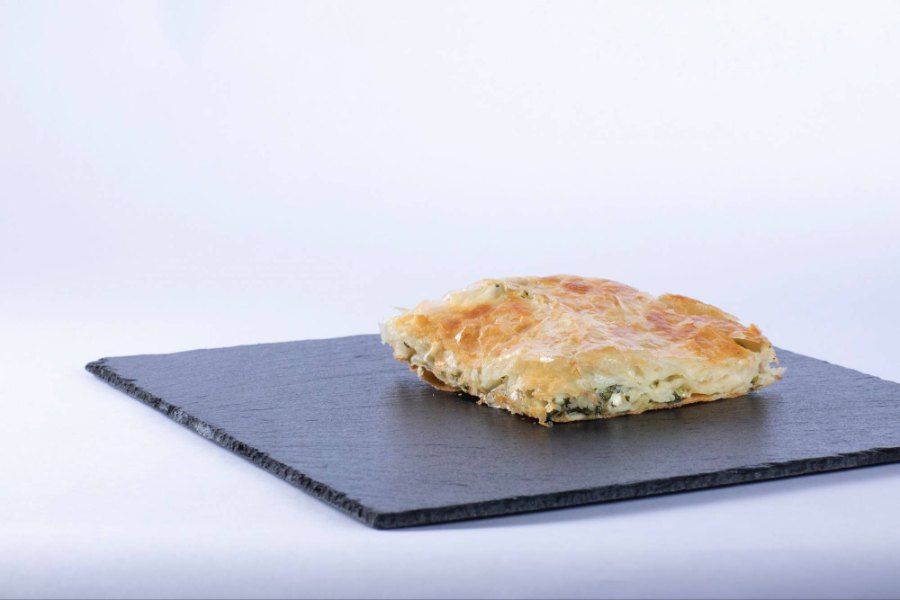 Auf einem Tisch steht ein Burek, aus dem ein Stück herausgeschnitten wurde.