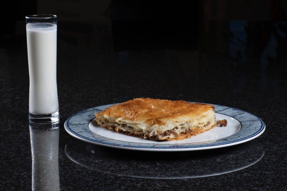 Ein Stück Burek auf einem Teller neben einem Glas Milch. Foto von der Burek House GmbH.