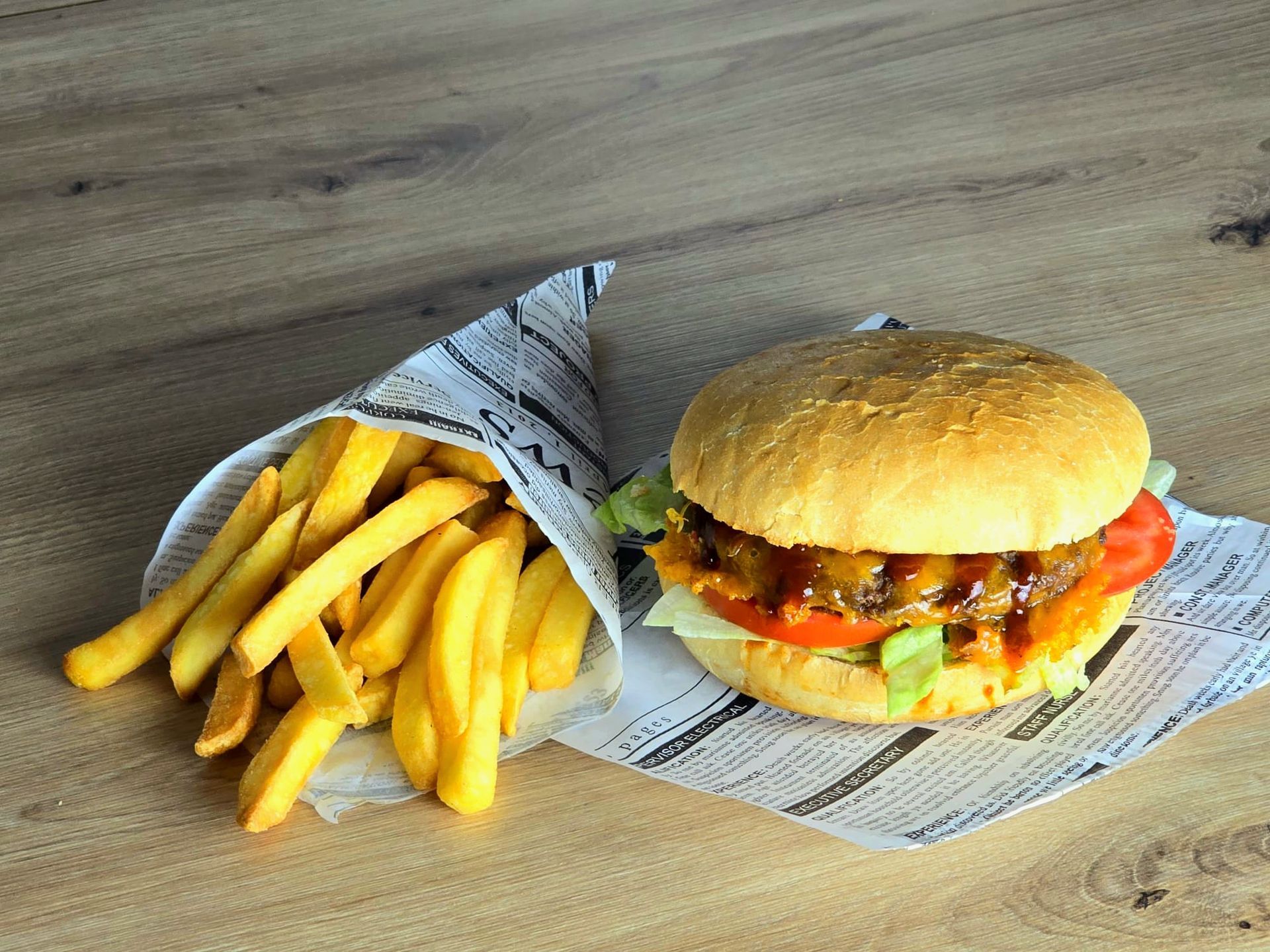 Ein Hamburger und Pommes Frites liegen in Zeitungspapier eingewickelt auf einem Holztisch.