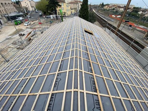 Toiture en construction avec poutres en bois apparentes et sous-toiture noire, à l'extérieur avec vue sur la ville.