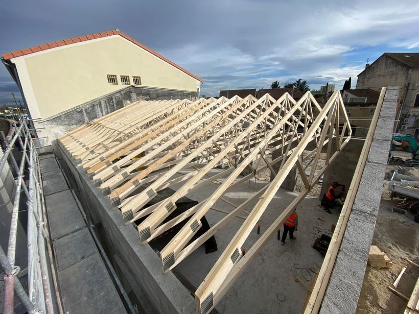 Construction de charpentes de toit en bois sur un bâtiment, présence d'ouvriers du bâtiment.