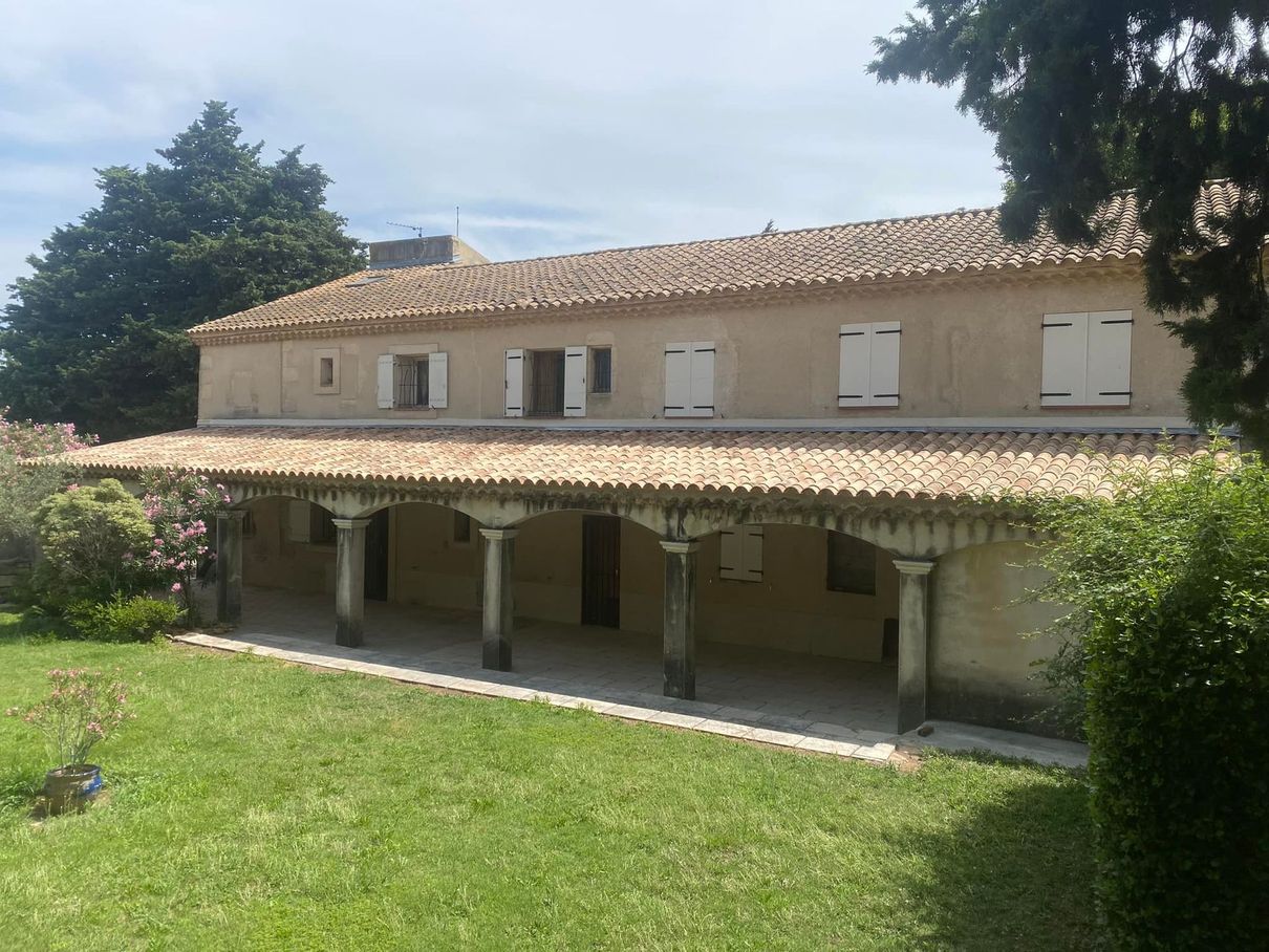 Bâtiment beige de deux étages avec toit de tuiles, colonnes soutenant un porche couvert, situé sur une pelouse verte.