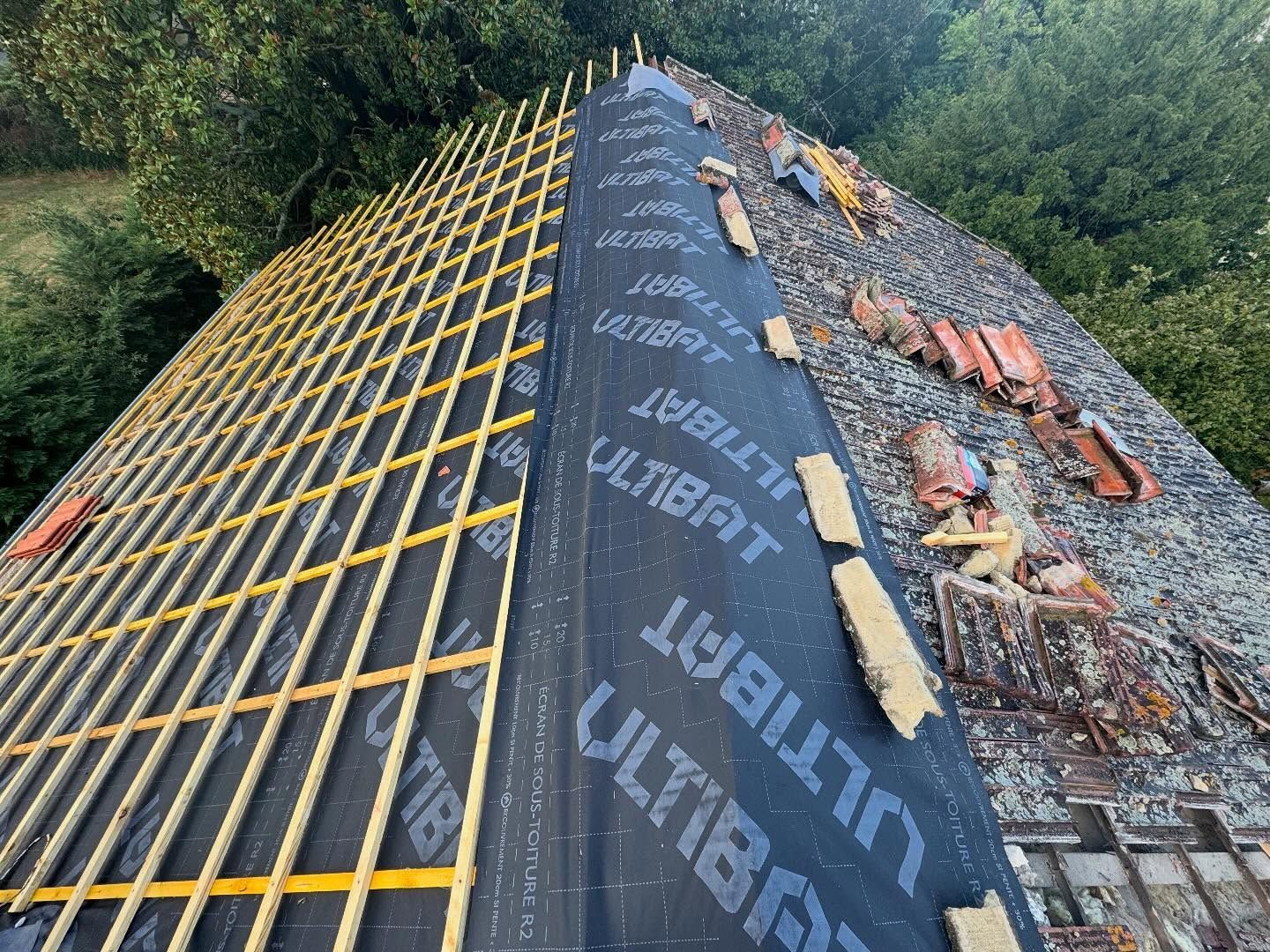 Toiture partiellement recouverte d'une nouvelle sous-couche, de nouvelles lattes de bois et de vieilles tuiles abîmées par les intempéries.