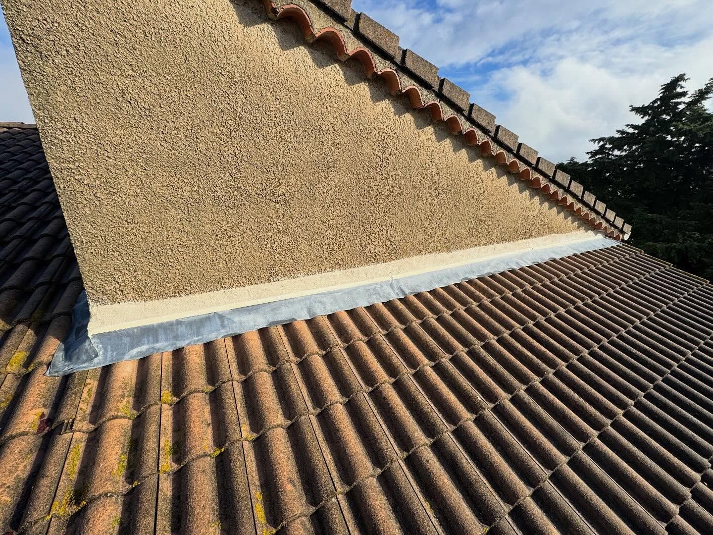 Gros plan sur un mur pignon en crépi rejoignant un toit de tuiles avec solin en plomb et bord de tuile de rive incurvé.