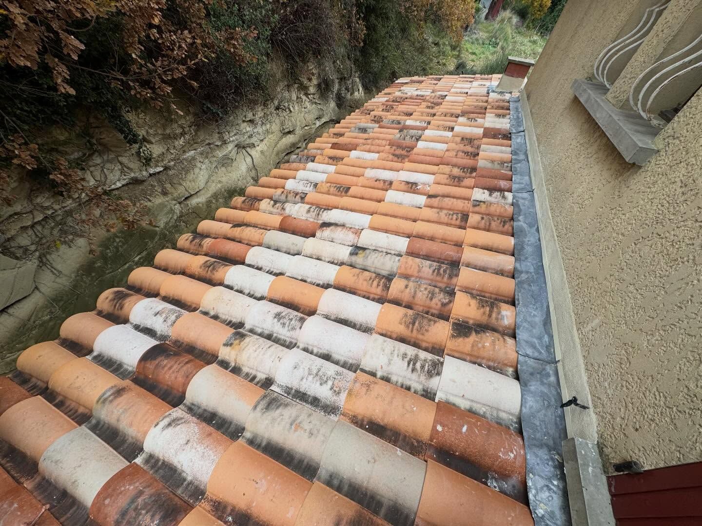 Toit de tuiles en terre cuite à côté d'un bâtiment beige avec une petite fenêtre.