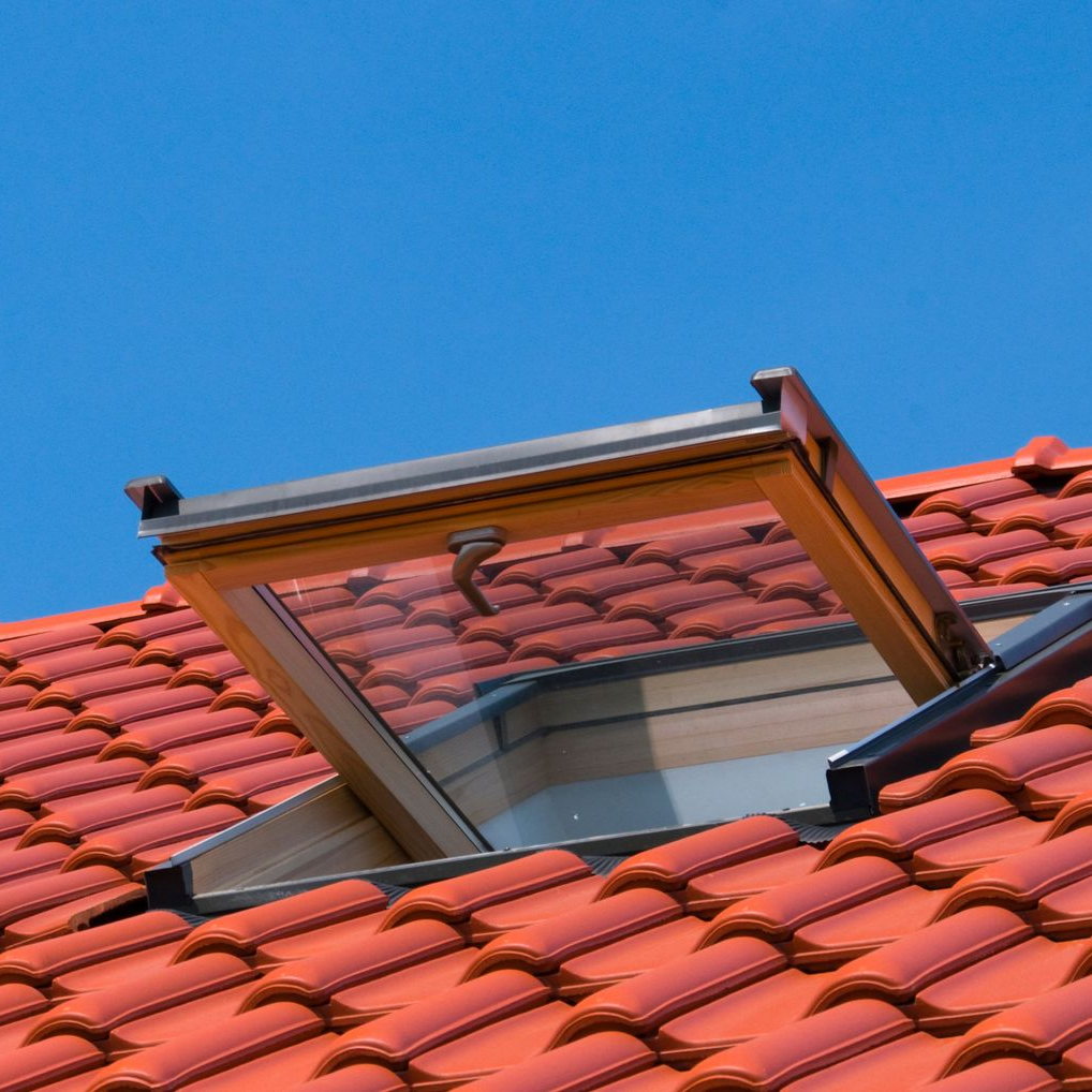Puits de lumière ouvert sur un toit de tuiles rouges se détachant sur un ciel bleu.