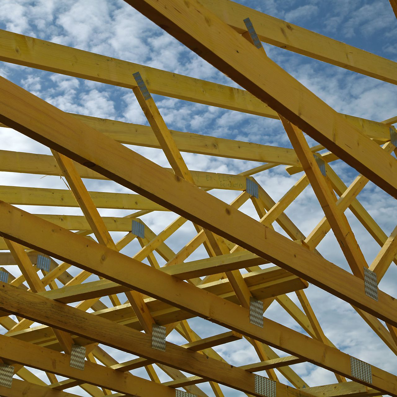Charpente de toit en bois se détachant sur un ciel partiellement nuageux.