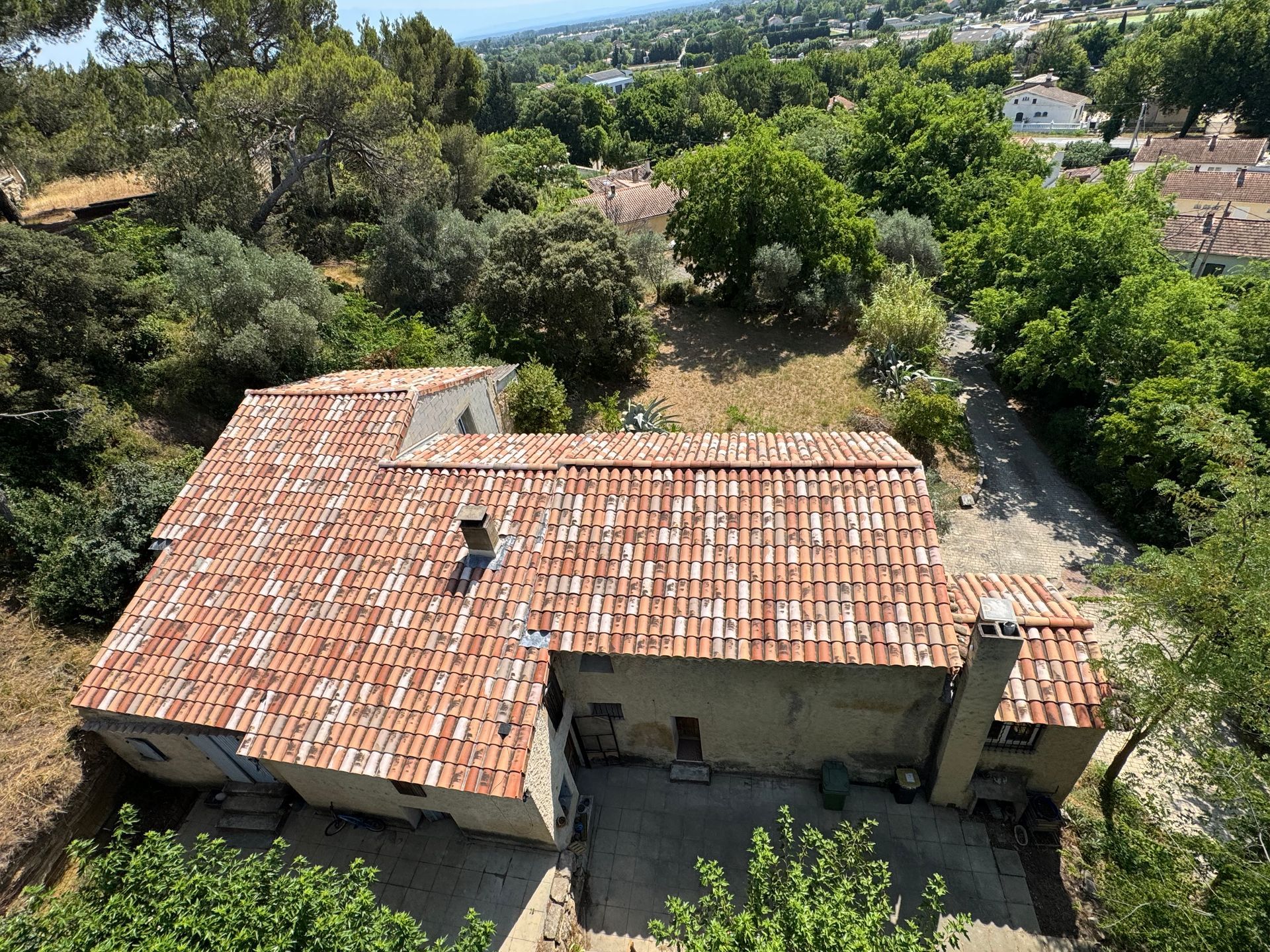 Toit de tuiles brunes, composé de deux pans se rejoignant au faîte, entouré de feuillage vert.