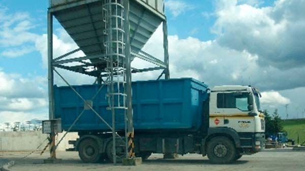 Un camión volquete azul está estacionado al lado de un silo.
