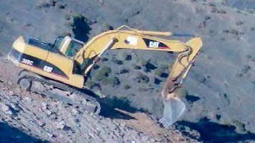 Una excavadora amarilla está sentada en la cima de una colina rocosa.