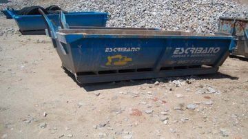 Un contenedor de basura azul está encima de una pila de grava.