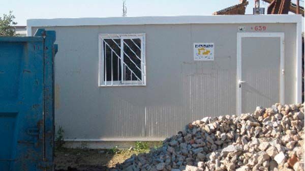 Un edificio con una ventana y una puerta está sentado al lado de una pila de rocas.