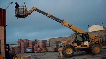 Un hombre está sentado en un cubo encima de una grúa.
