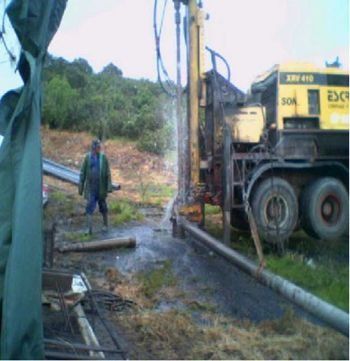 Un hombre con una chaqueta verde está de pie junto a una excavadora amarilla.