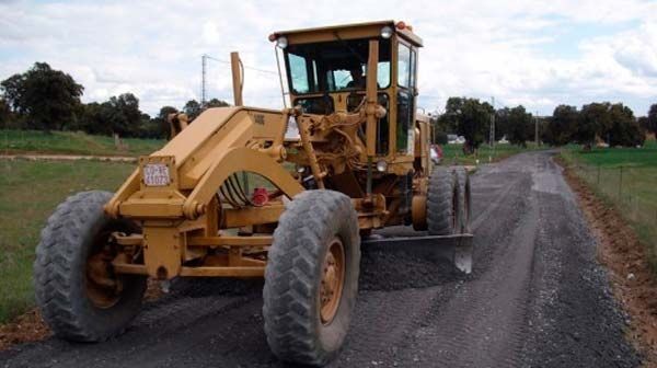 Un tractor amarillo conduce por un camino de tierra.