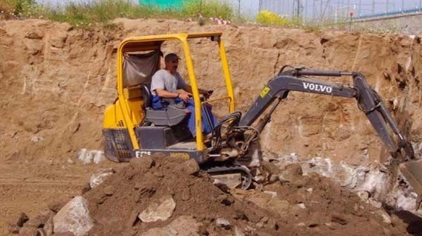 Un hombre conduce una excavadora Volvo en un campo de tierra.