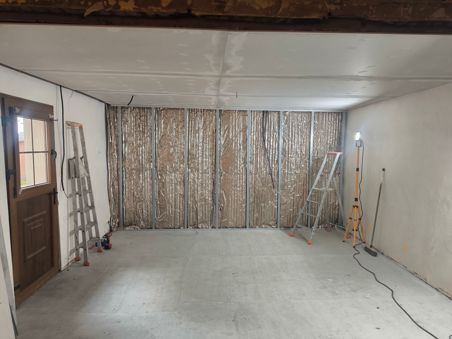 Pièce intérieure en rénovation, charpente apparente, isolation, outils, murs non finis, porte.