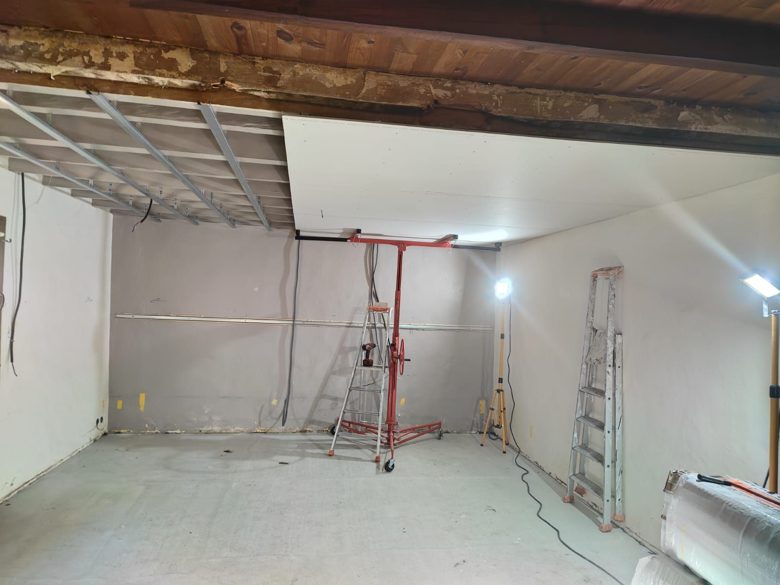 Rénovation intérieure : pose de plaques de plâtre sur un plafond à ossature métallique. Présence d’une échelle et d’une nacelle élévatrice.