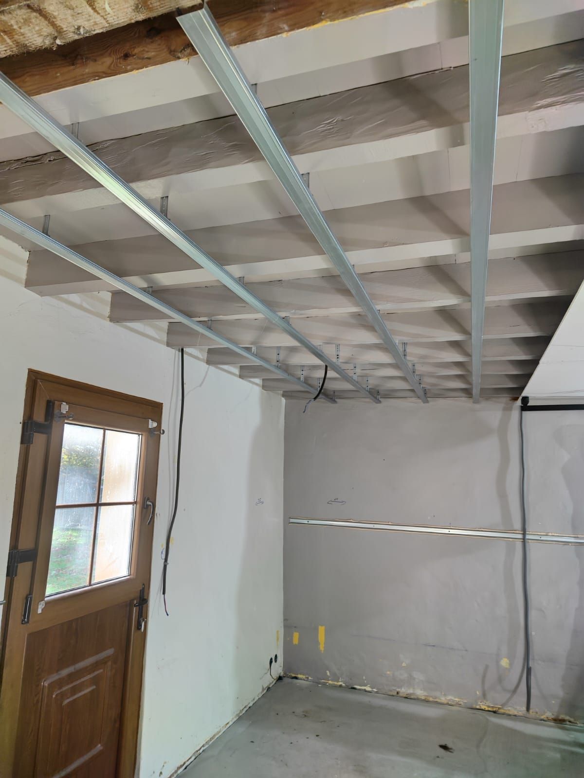 Intérieur d'une pièce avec un plafond à ossature métallique. Porte à gauche, murs gris.