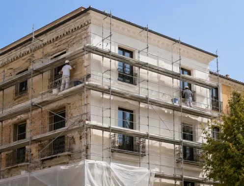 Fachada del edificio cubierta de andamios durante las obras de renovación, con trabajadores en el exterior.