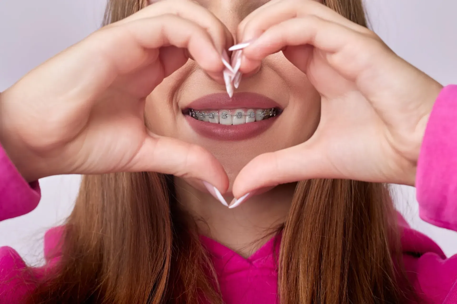 Persona con brackets haciendo forma de corazón con las manos, sonriendo.