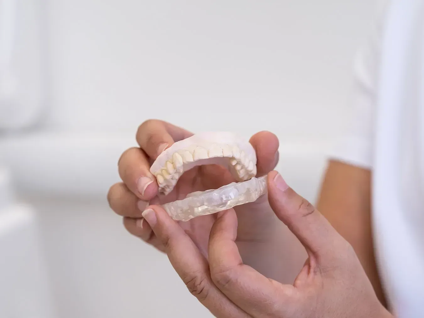 Persona sosteniendo dos alineadores dentales transparentes, uno para cada mandíbula, en un entorno médico.