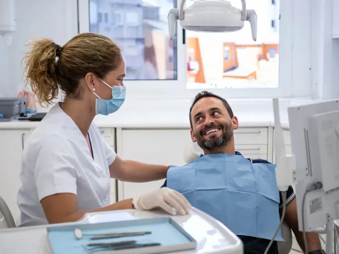 Un dentista con mascarilla y guantes consuela a un paciente con la mano en el hombro en el consultorio dental.