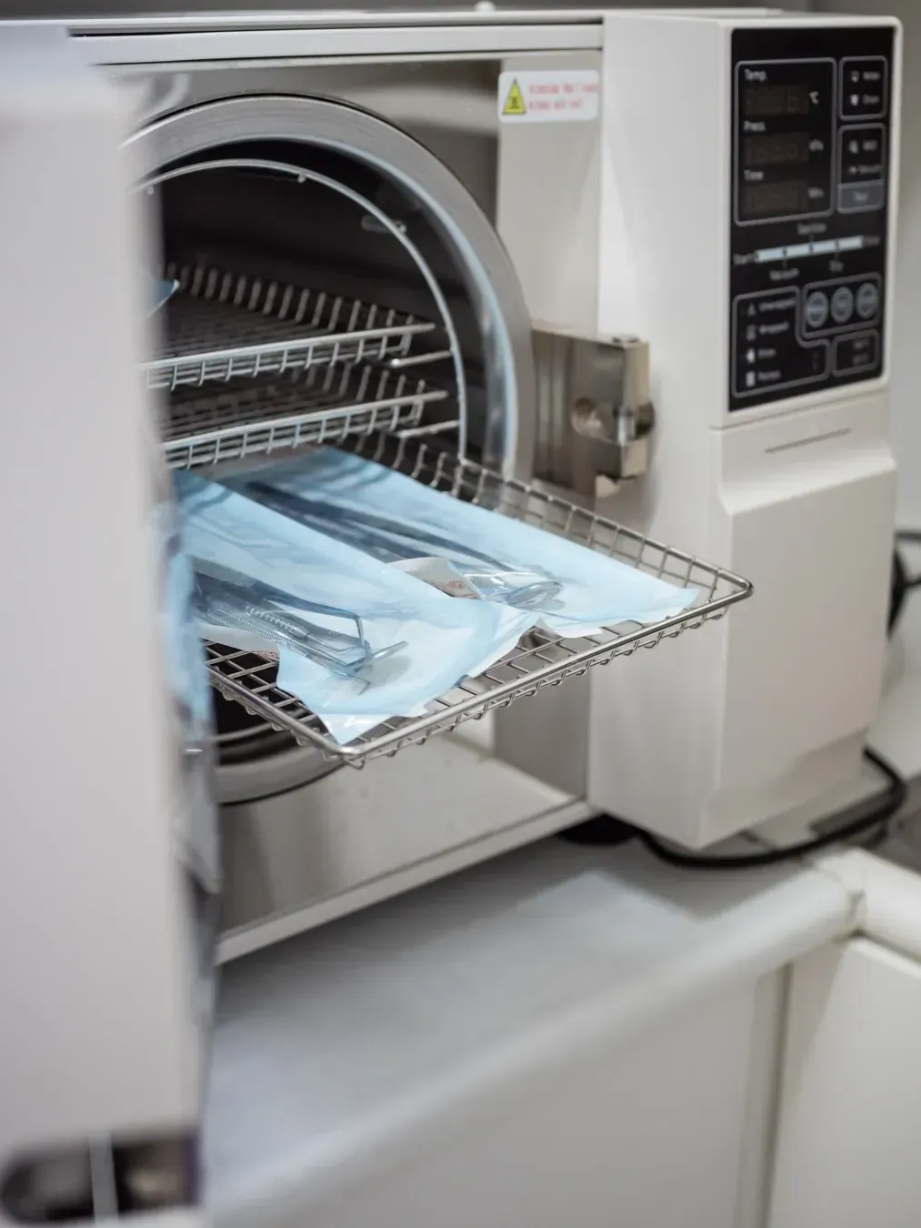 Autoclave con bandeja de instrumentos quirúrgicos sellados en su interior, en un entorno médico.