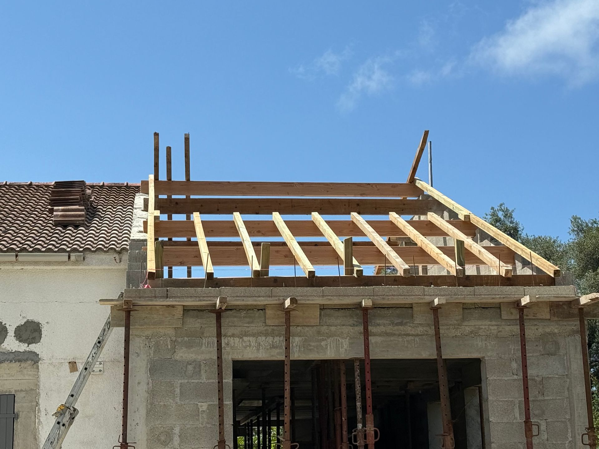Maison partiellement construite avec charpente de toit en bois apparente sous un ciel bleu