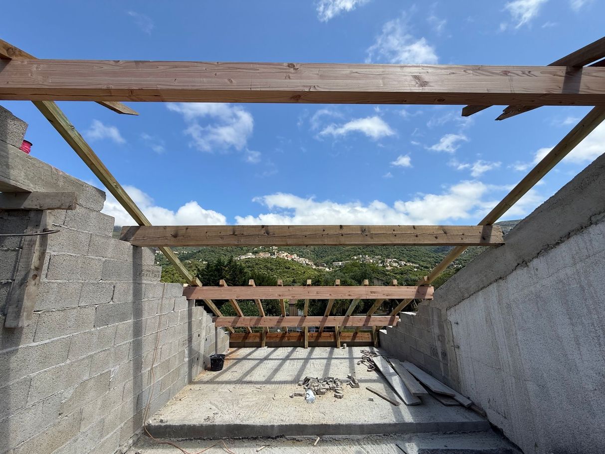 Passerelle en béton sur le toit en construction, avec des poutres en bois encadrant un ciel bleu