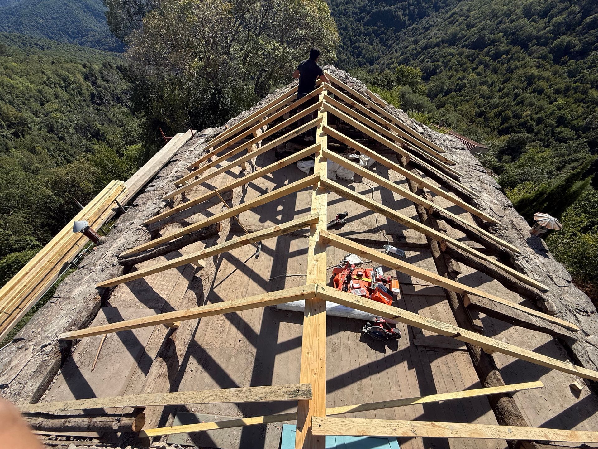 Charpente de toit en bois en construction sur un versant escarpé avec des montagnes en arrière-plan