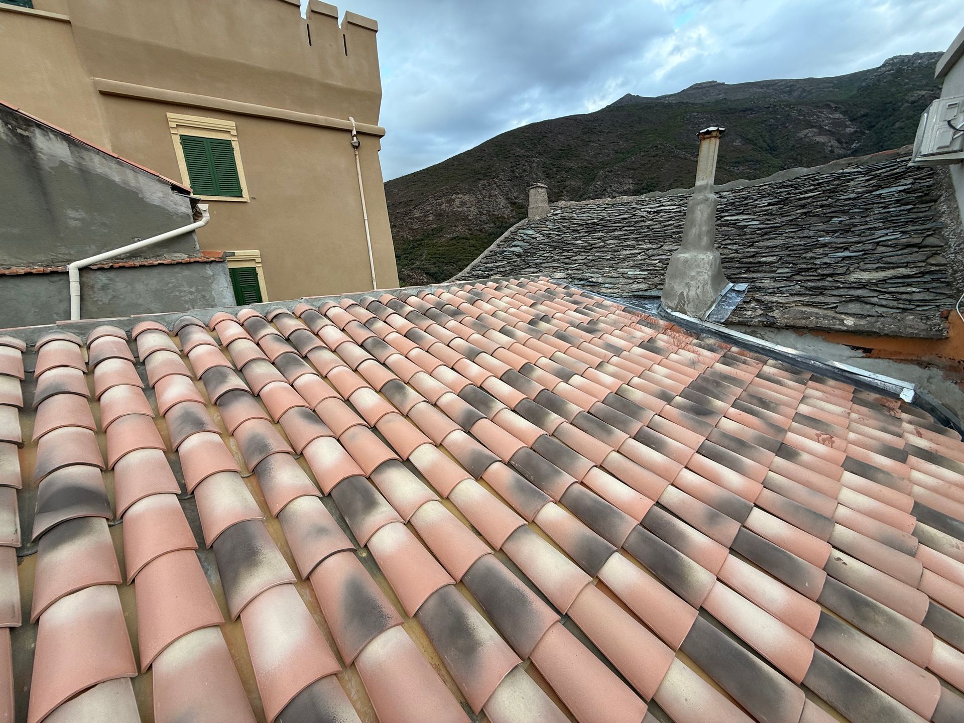 Toit de tuiles en terre cuite rouge à côté d'un bâtiment beige et d'un mur de pierre.