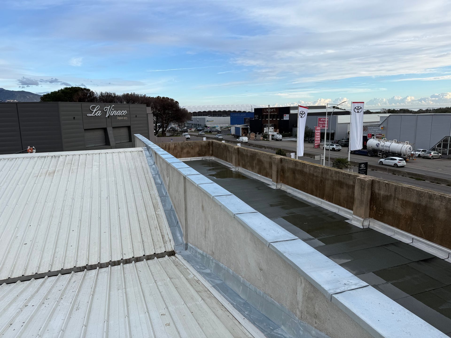 Vue du toit d'une zone industrielle avec toiture métallique et camions stationnés sous un ciel nuageux