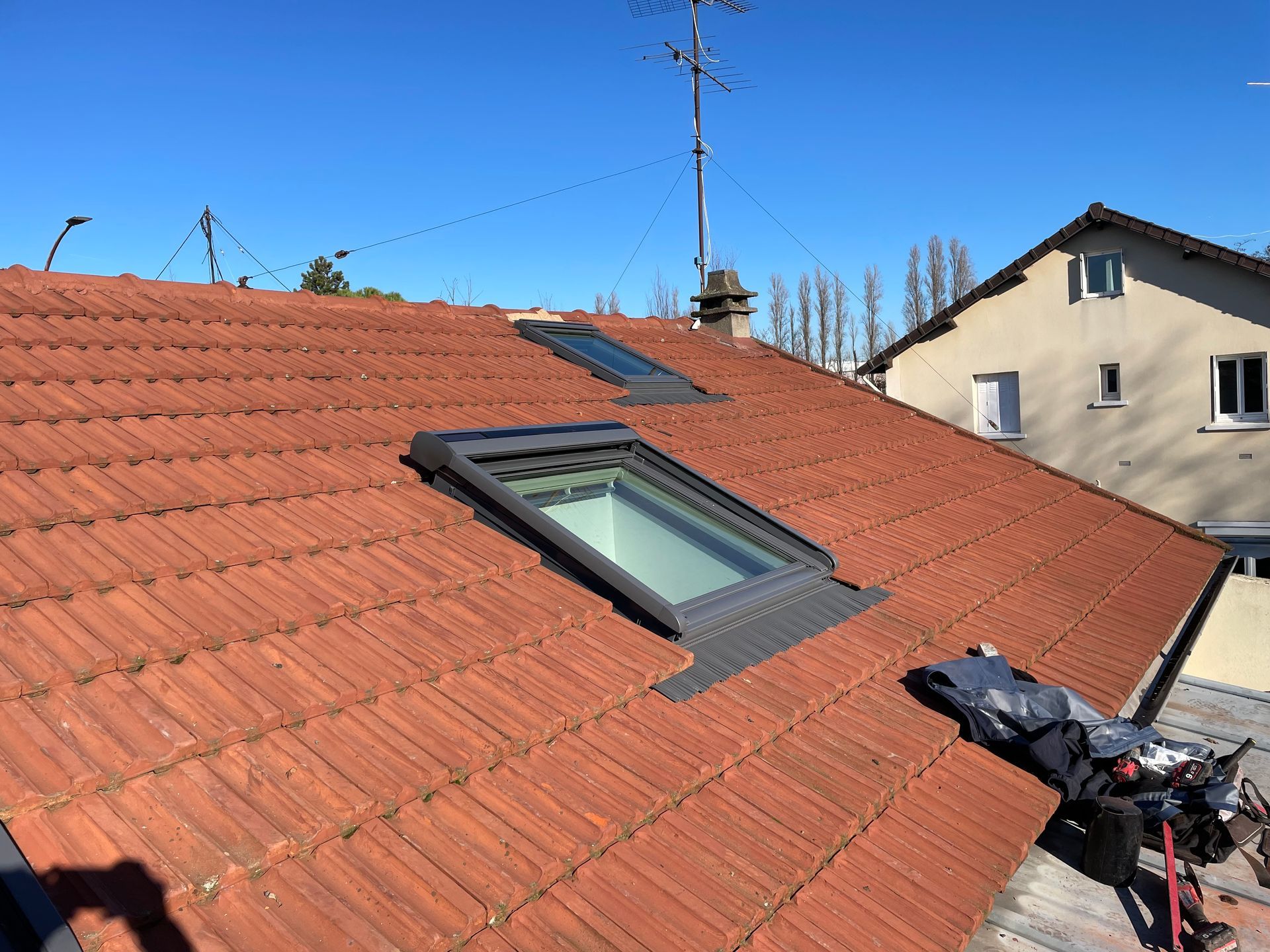 Toit de tuiles rouges avec puits de lumière et panneaux solaires.