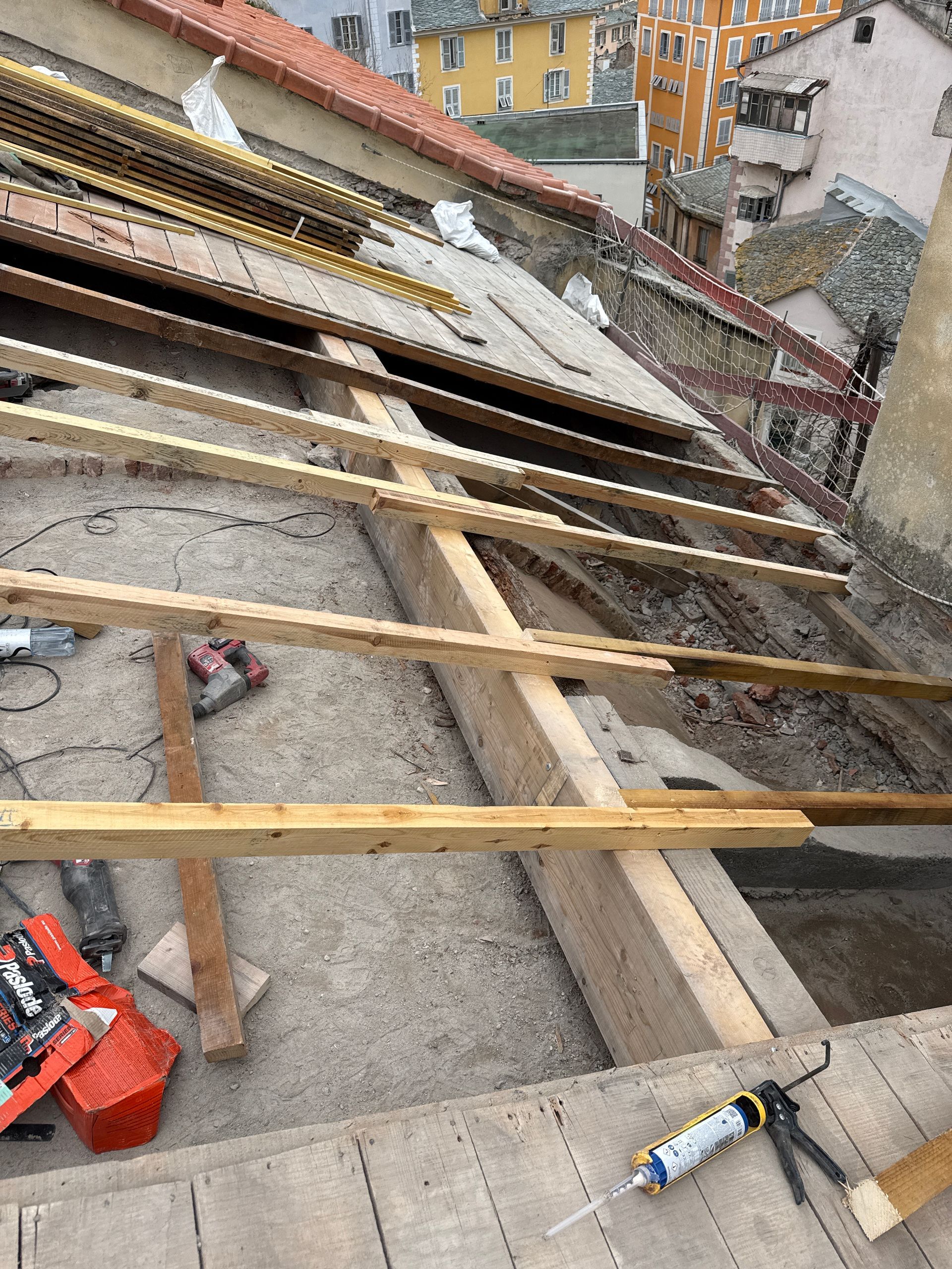 Travaux de construction de toiture avec des poutres en bois au-dessus d'un toit pentu et des outils.