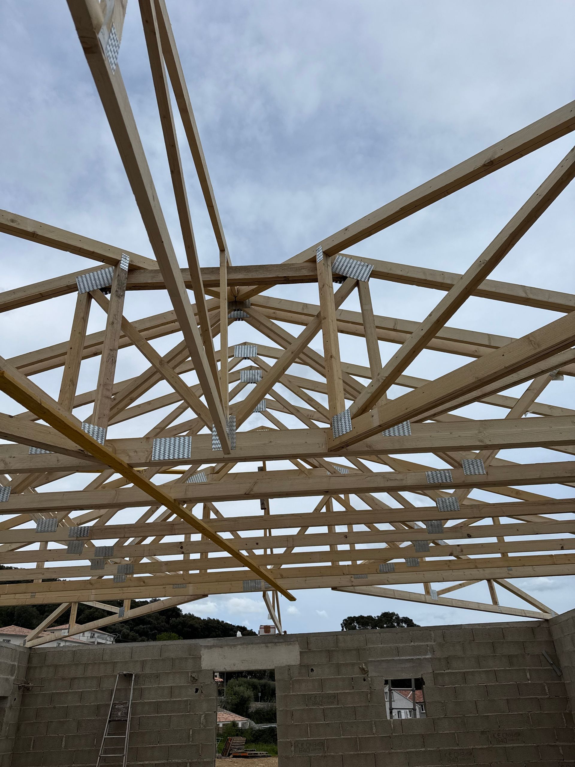Charpente de toit en bois en construction au-dessus de murs en parpaings, vue de l'intérieur d'un bâtiment inachevé.