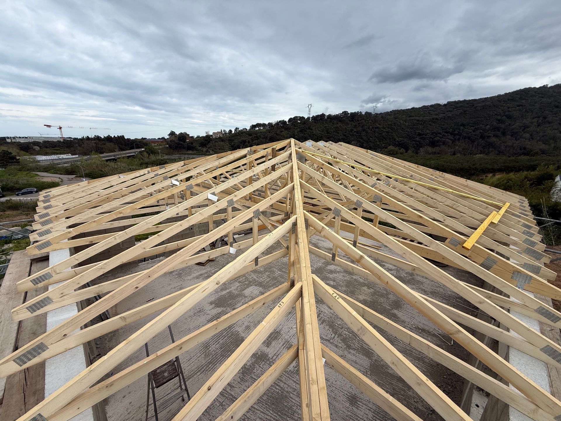 Charpente en bois d'un bâtiment en construction, vue depuis la crête sur fond de ciel nuageux.