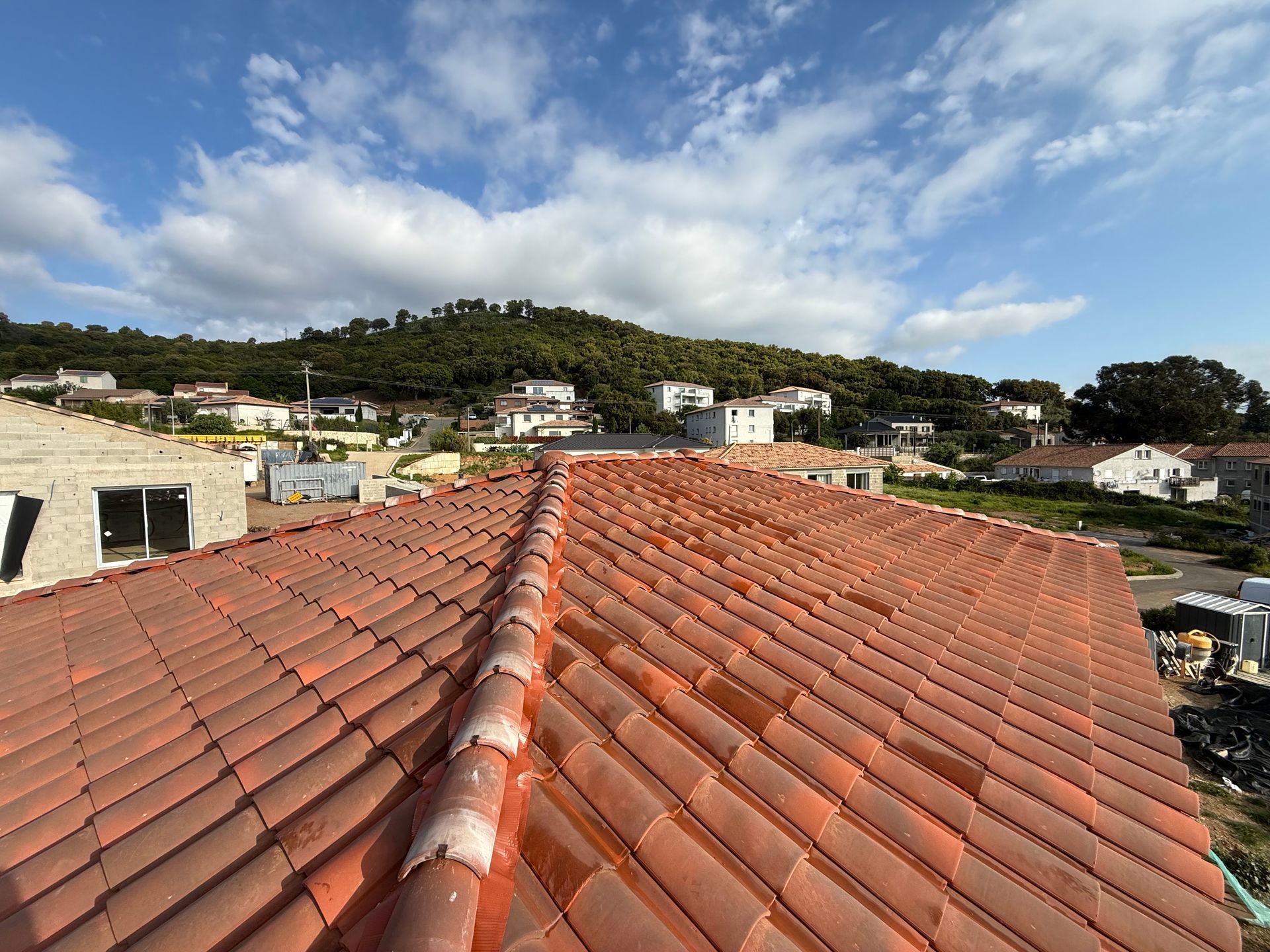 Toiture en tuiles de terre cuite rouge surplombant un quartier à flanc de colline sous un ciel bleu parsemé de nuages