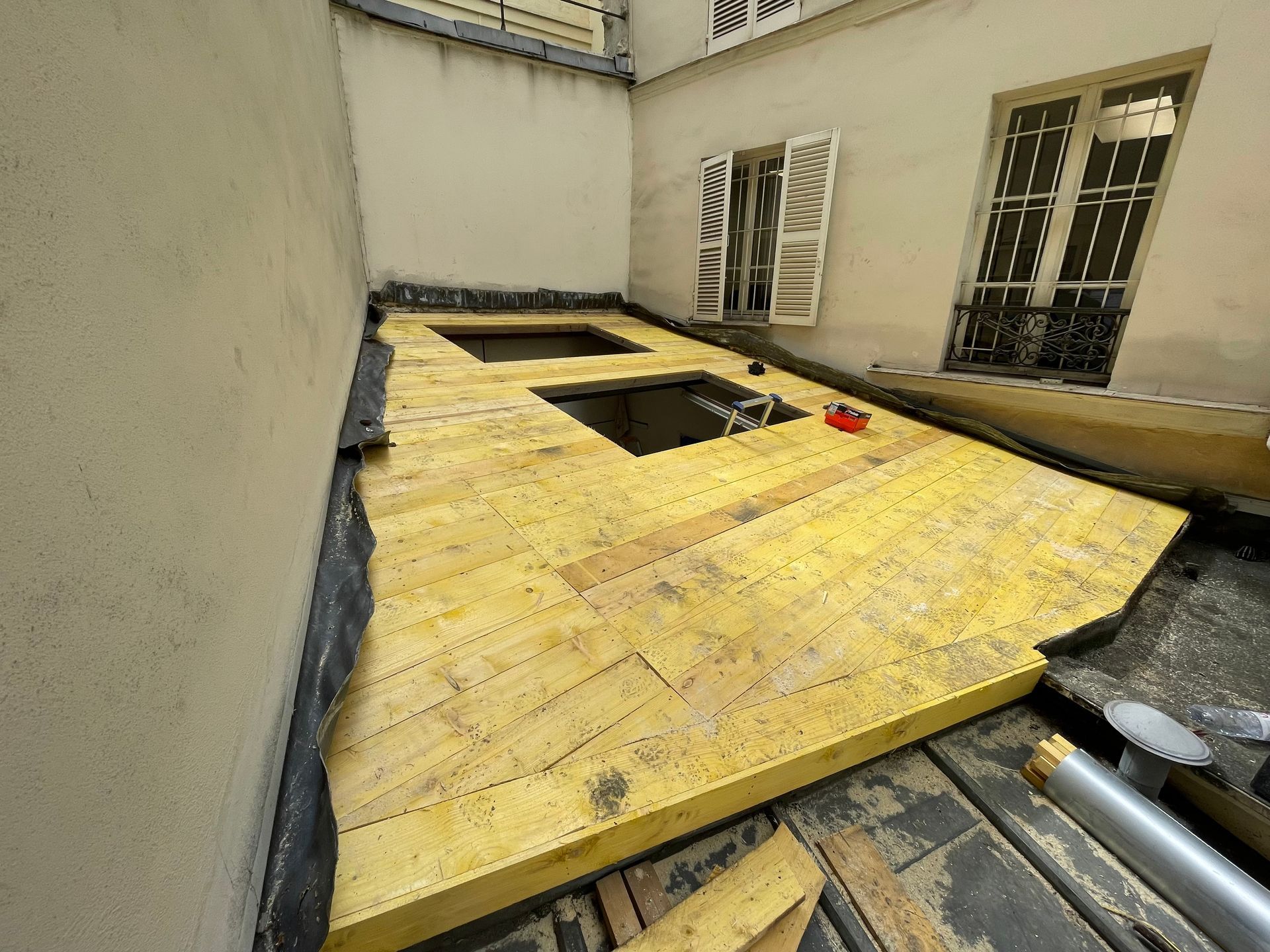 Panneaux de contreplaqué jaune au-dessus d'une ouverture dans une pièce aux murs et fenêtres beiges