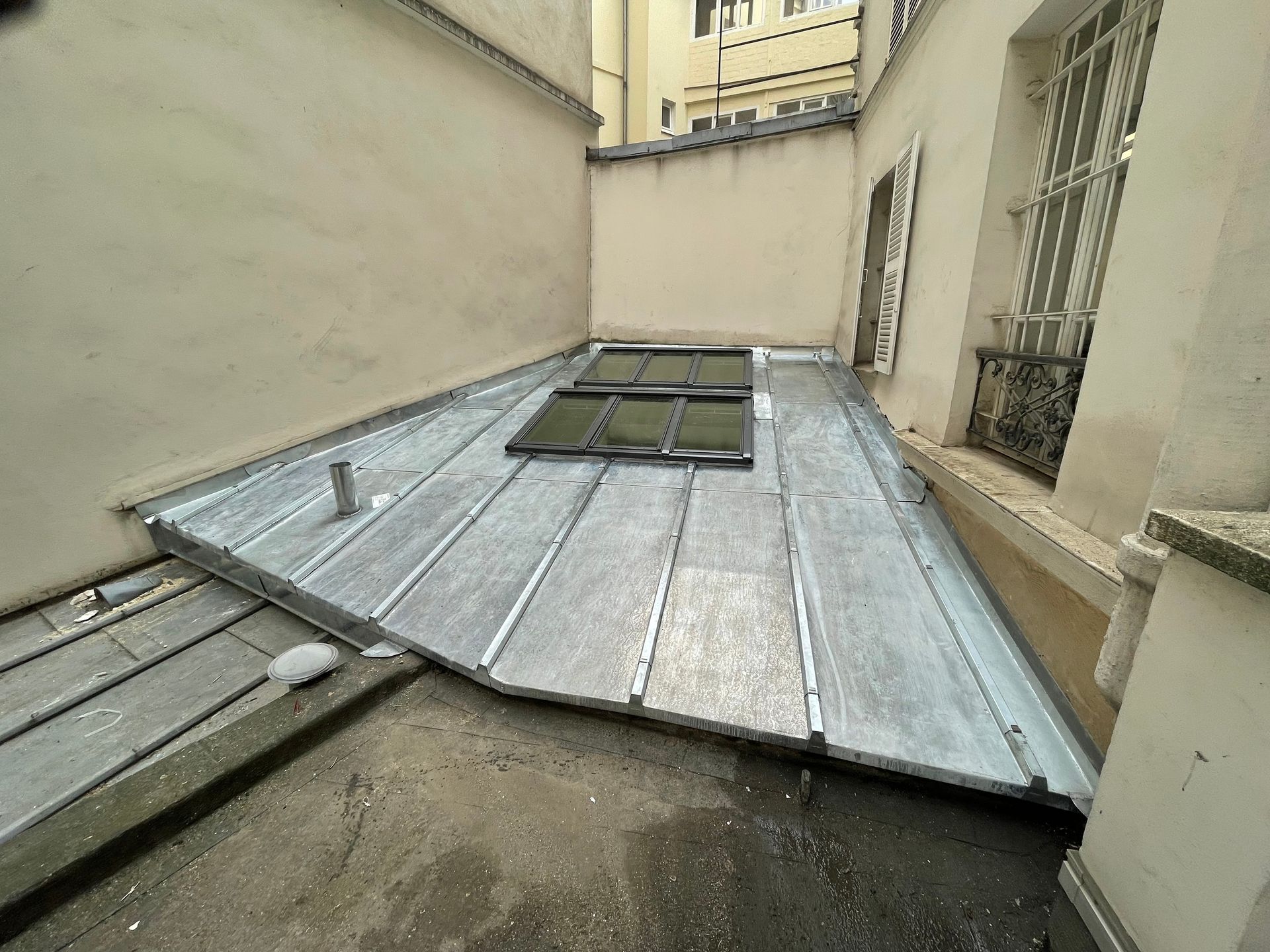 Panneaux de toiture métalliques recouvrant une étroite passerelle sur le toit entre des bâtiments beiges