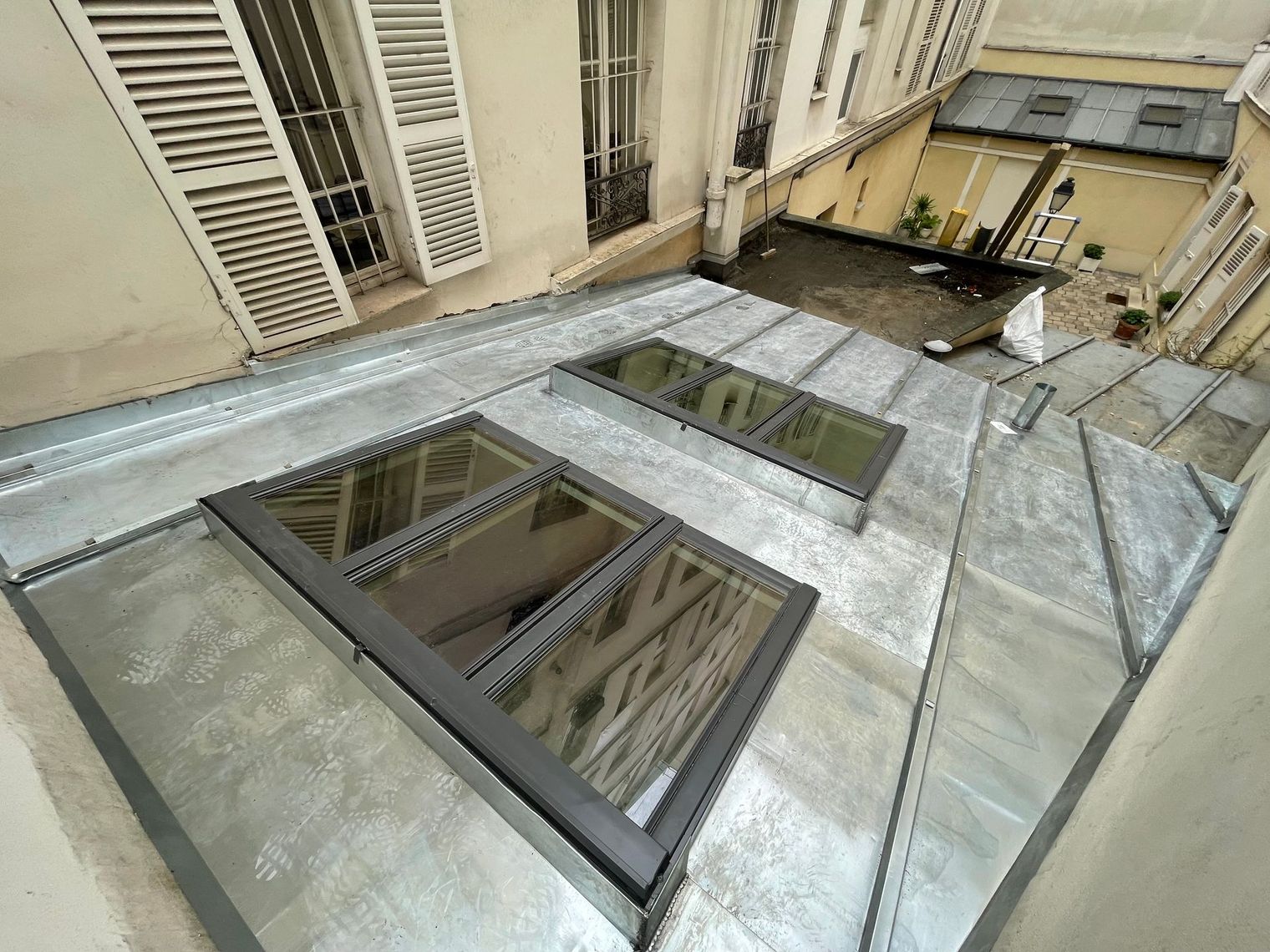 Toiture avec plusieurs puits de lumière et aérations métalliques à côté d'un mur de bâtiment