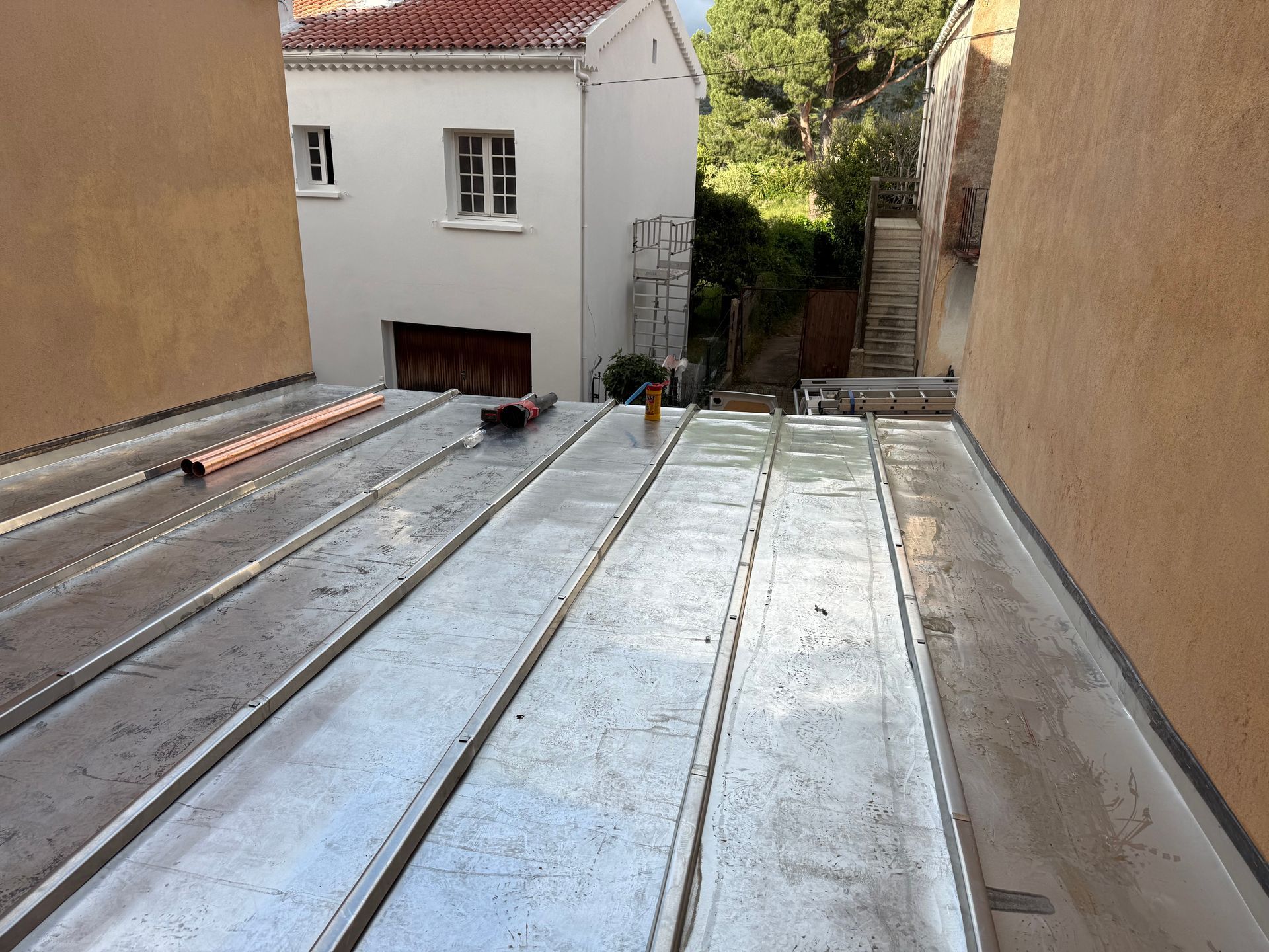 Panneaux de toiture métalliques dans une ruelle étroite entre des bâtiments, avec une maison blanche.