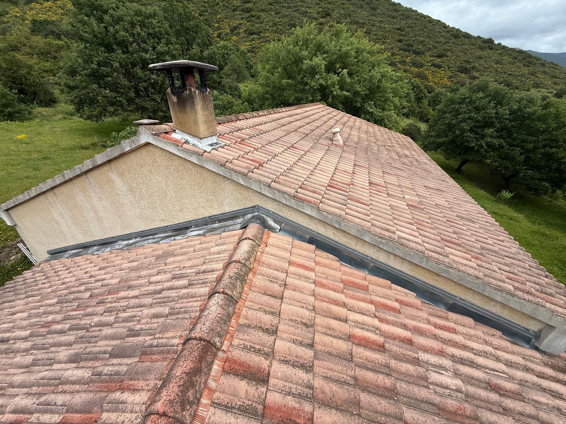 Toit de tuiles rouges avec cheminée et collines verdoyantes en arrière-plan