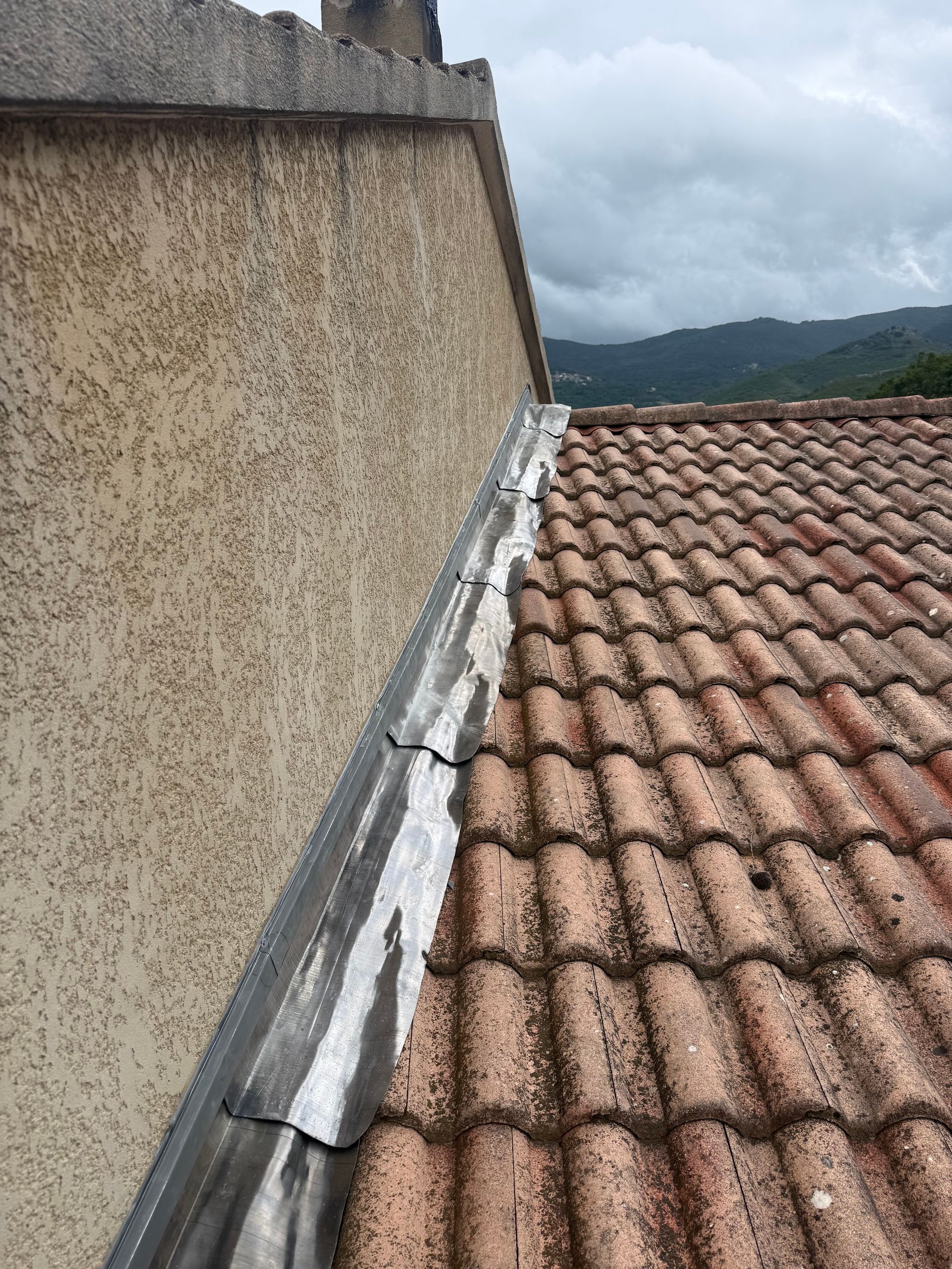Toiture en tuiles de terre cuite rouge, mur en stuc patiné et arrière-plan montagneux nuageux