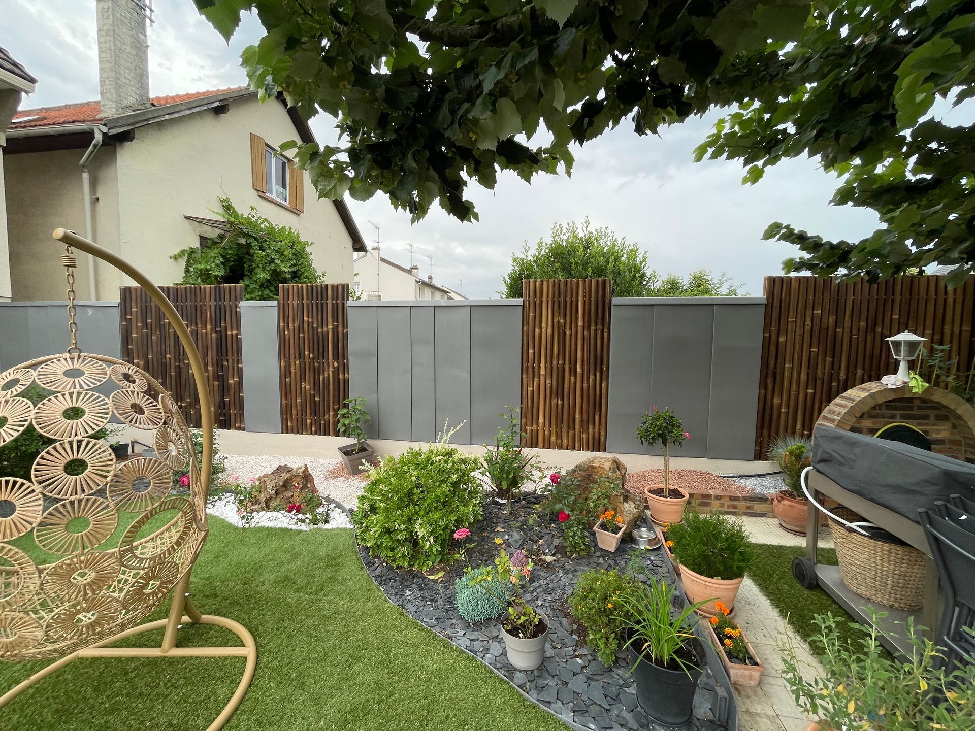 Jardin arrière avec fleurs en pot, pelouse verte, clôture en bois et mobilier de jardin sous un arbre