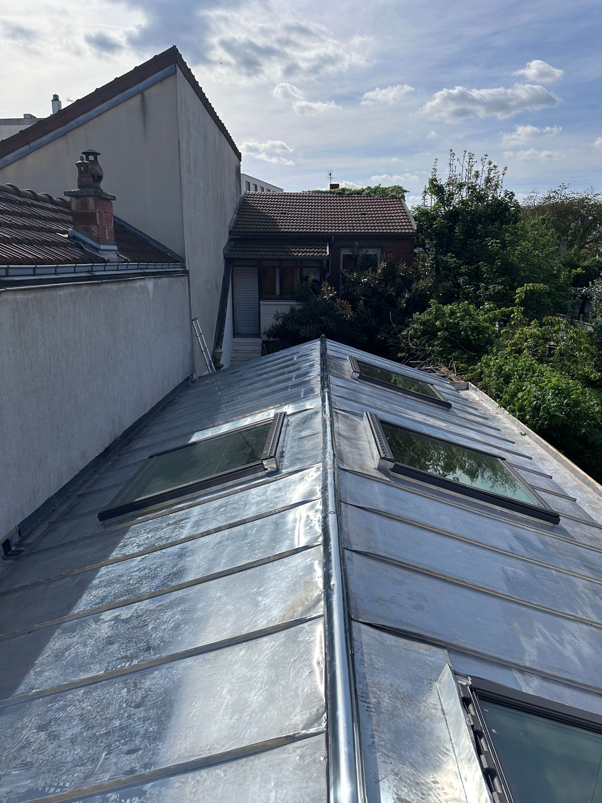 Vue depuis le toit d'une verrière à côté d'une maison blanche sous un ciel nuageux.