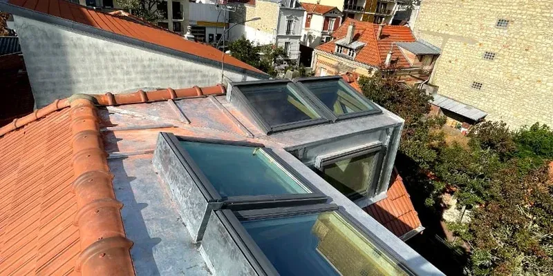 Puits de lumière avec cadres métalliques sur un toit en pente de tuiles rouges à côté des bâtiments