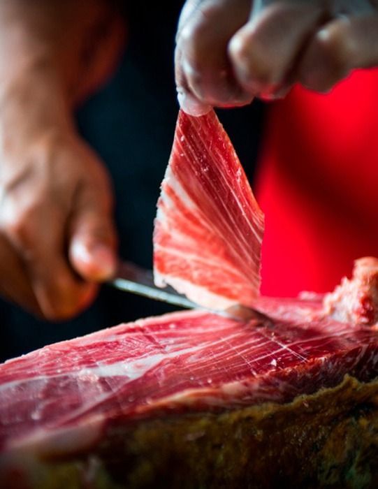 Manos cortando finas lonchas de carne roja sobre una tabla de cortar.