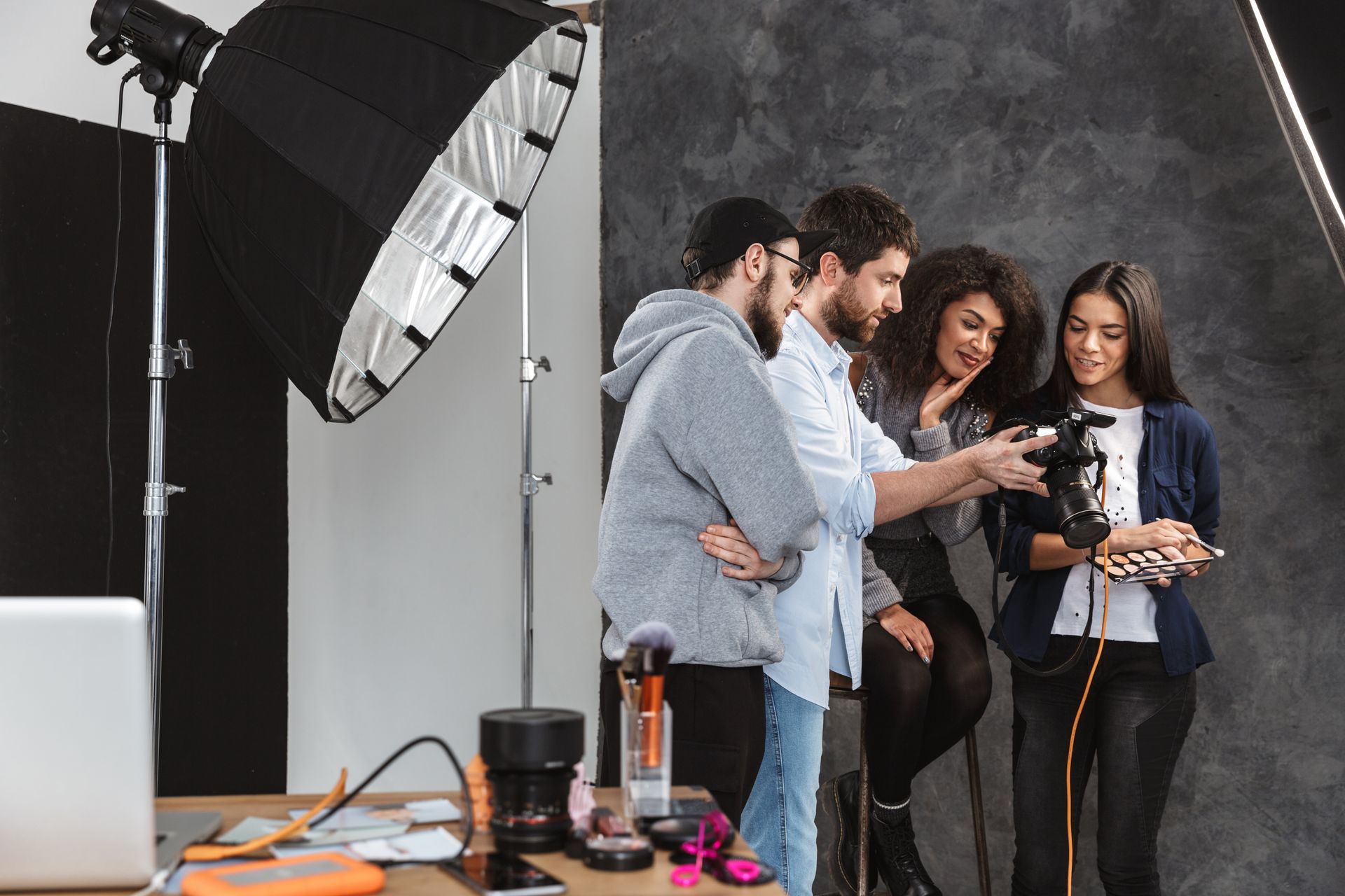 Quatre personnes dans un studio photo regardent un appareil photo ; on aperçoit une boîte à lumière, un fond et du matériel